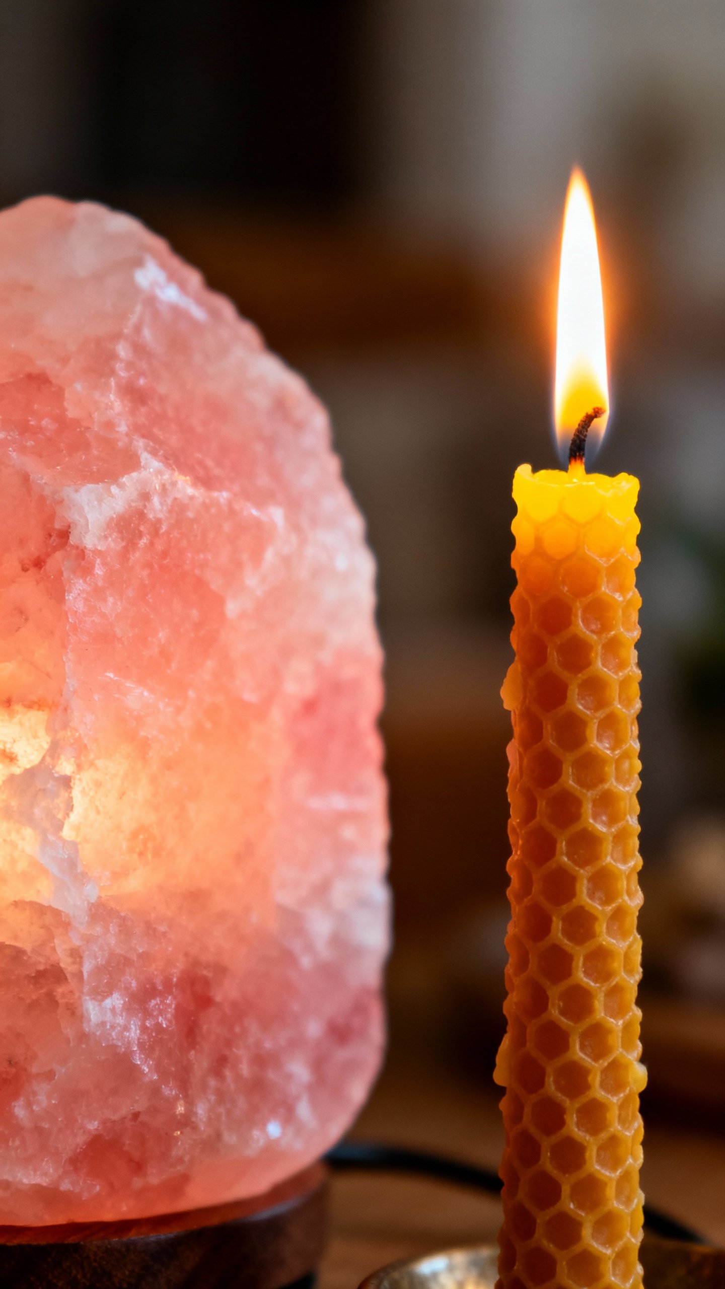 Closeup of beeswax candle flame beside salt lamp, warm 2700K glow