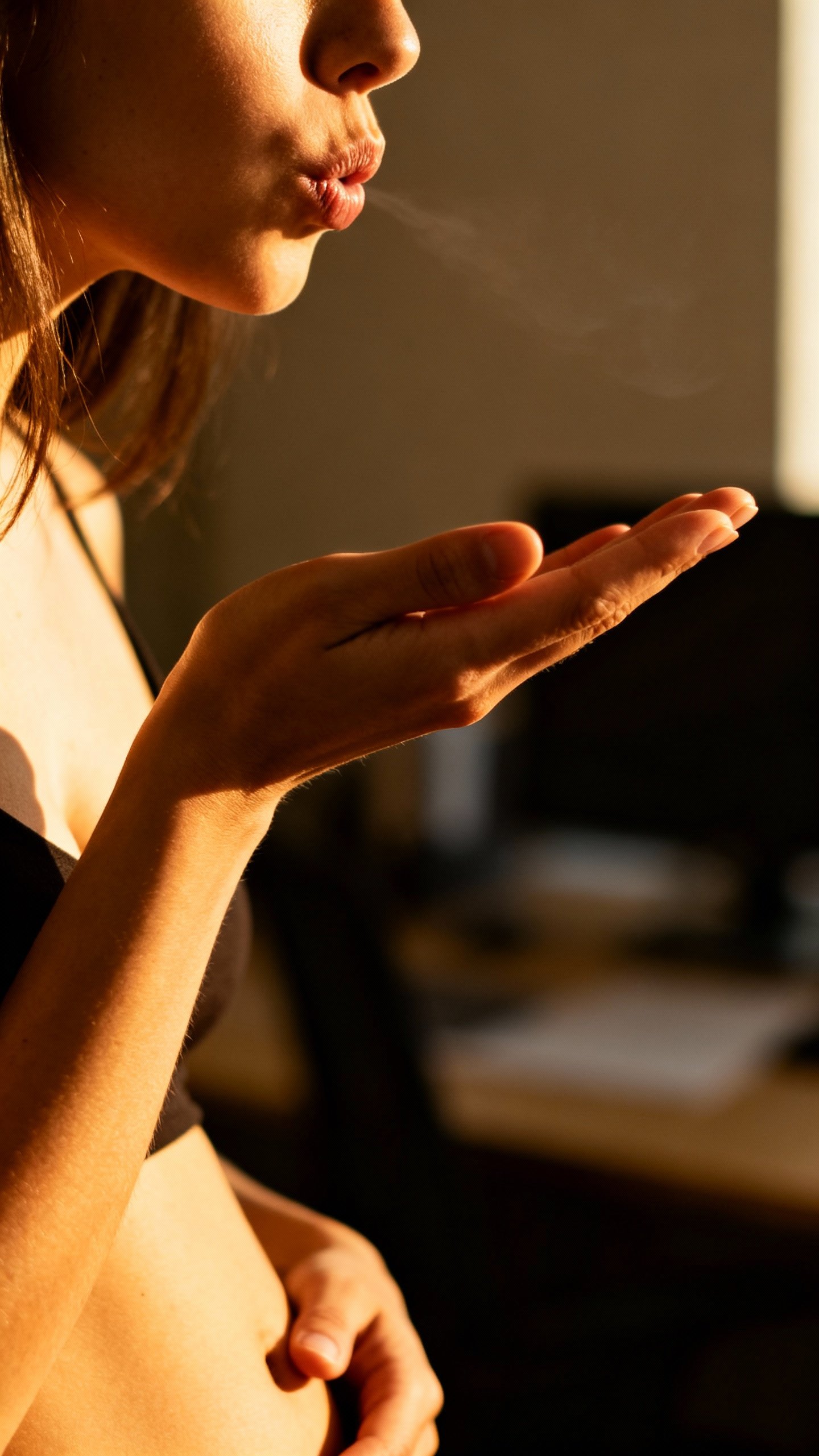 Closeup of female hands, pursed lips exhale, soft belly, warm office light