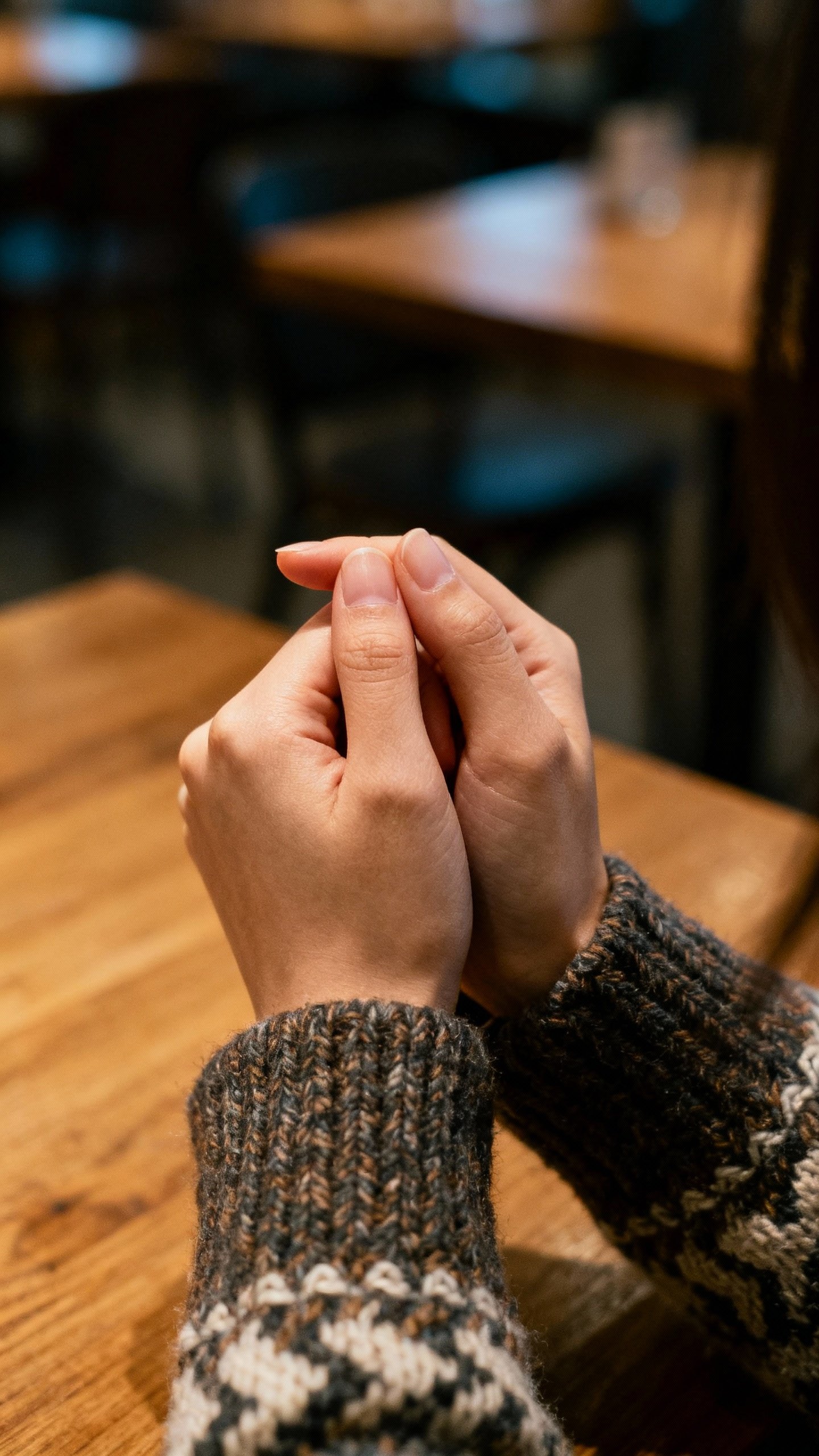 Female hands pressing thumb and index finger together, textured sweater sleeve, subtle cafe backgrou