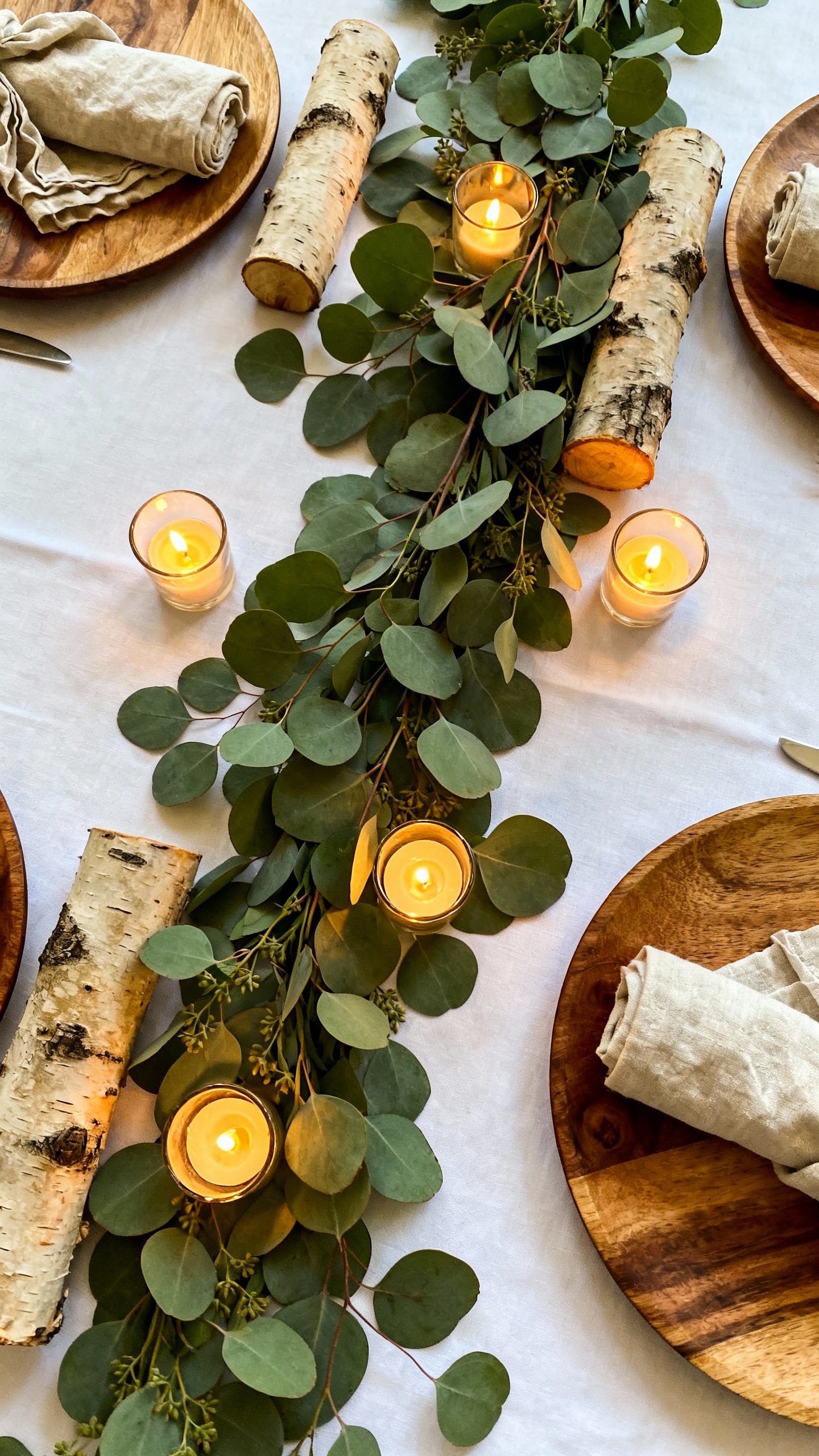 Overhead of eucalyptus greenery runner with tea lights, birch logs, linen napkins, wood chargers on