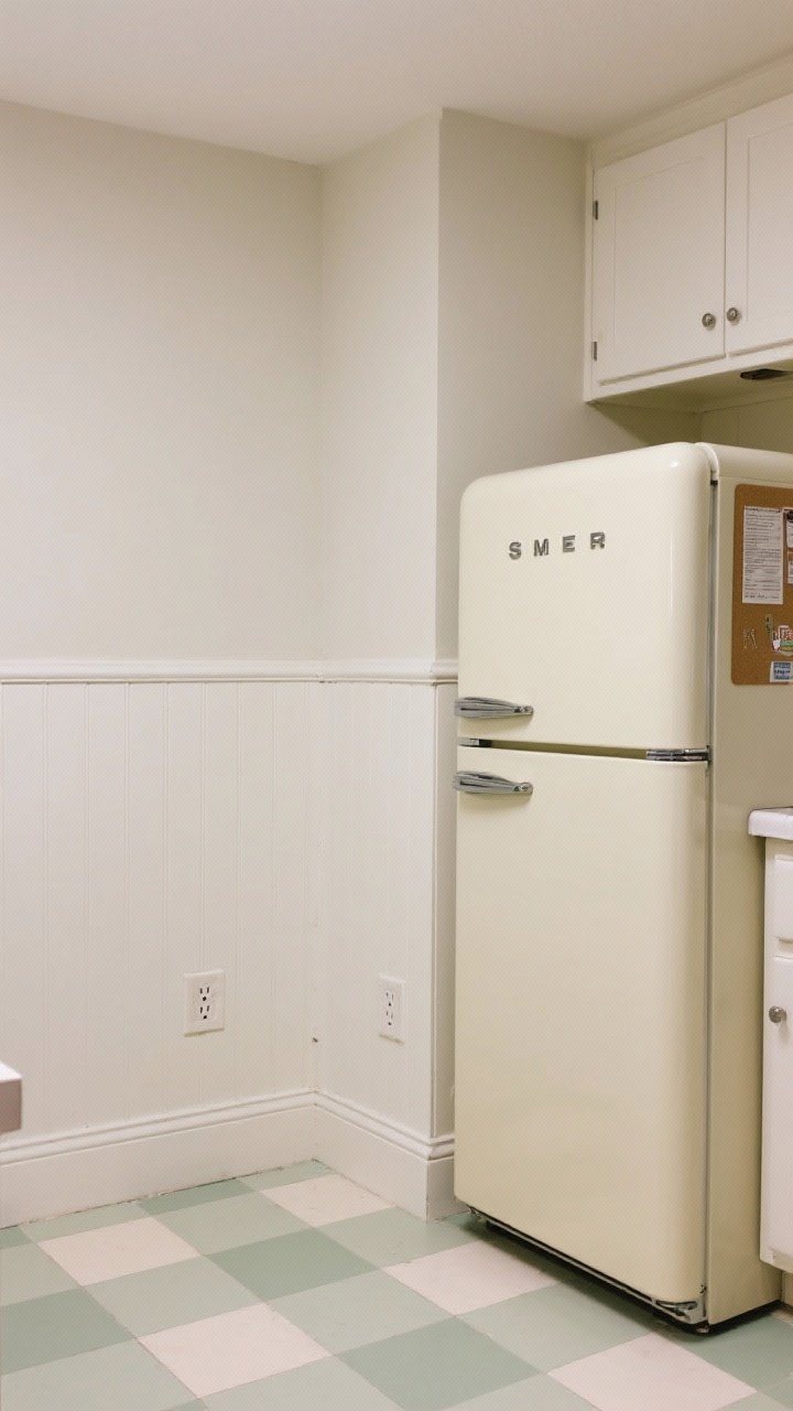 Medium, straight-on view of a renter kitchen corner featuring peel-and-stick transformations: matte beadboard-look backsplash in warm white, patterned vinyl floor tiles in soft sage-and-cream checks, and a cream magnetic appliance wrap giving a Smeg-adjacent pastel vibe on the fridge; neat outlet cutouts and caulk strip finishing for a built-in look; gentle ambient light, no glare.