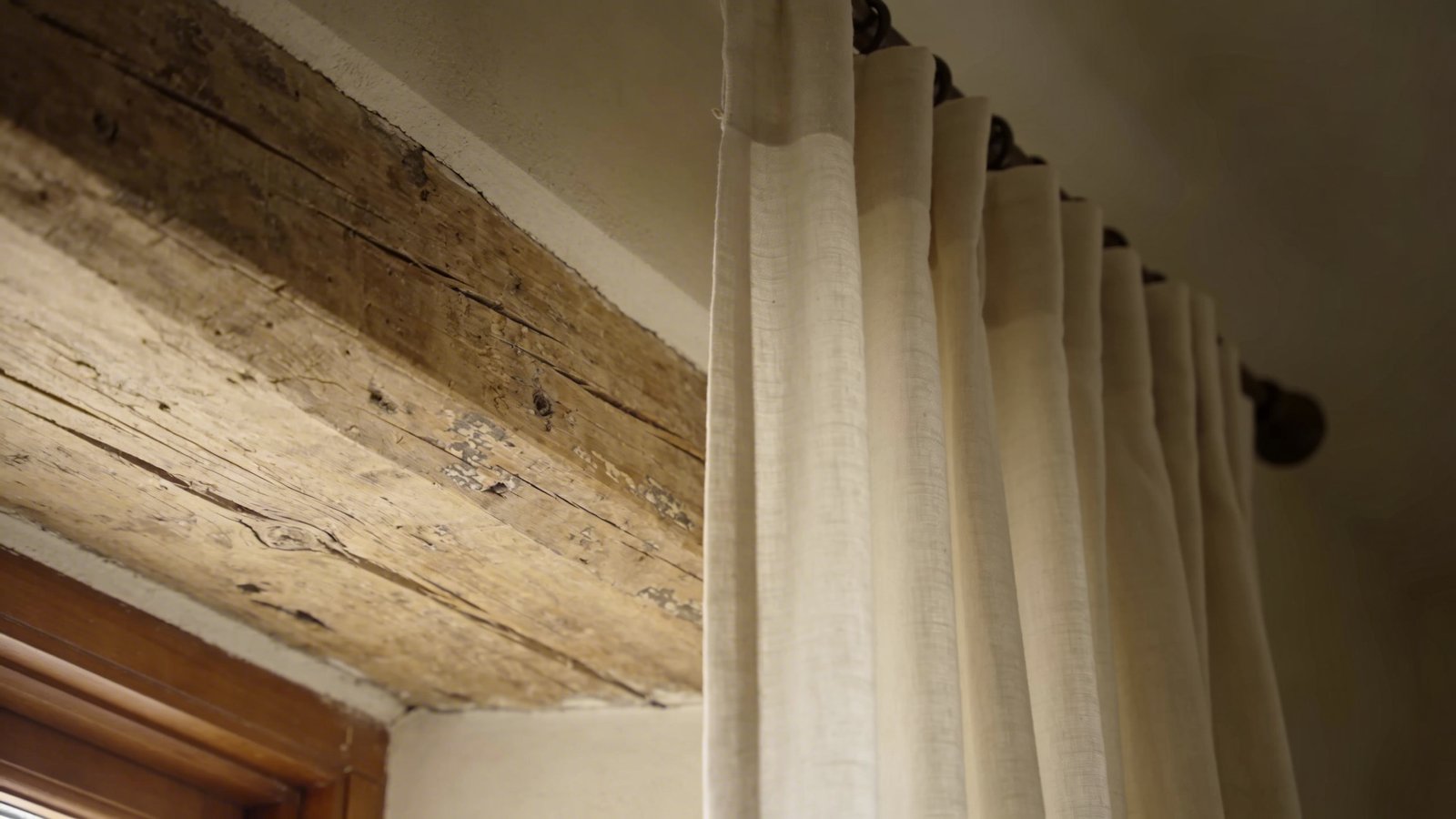 Aged wooden beam, soft neutral curtains, natural light.