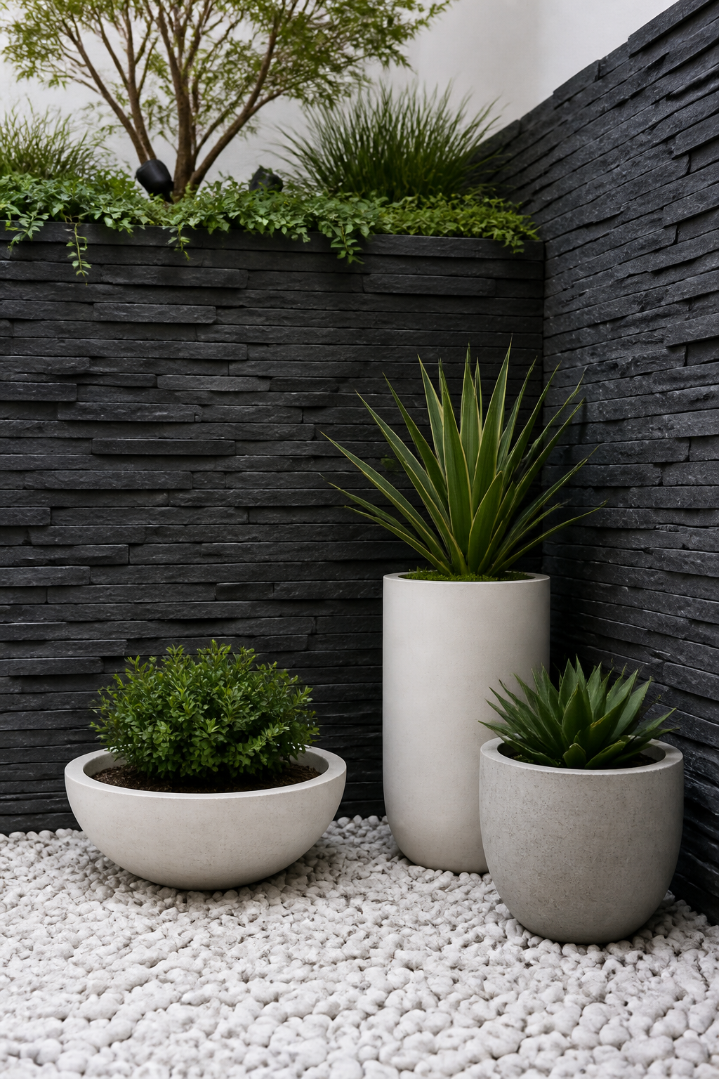 Compact urban garden corner showcasing stacked slate stone retaining wall in charcoal gray, paired with white gravel ground cover and three architectural planters with simple greenery, clean modern aesthetic, tight framing
